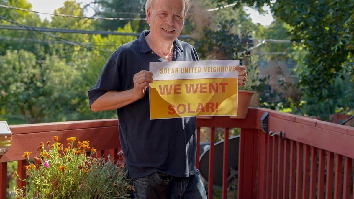 Man standing in his backyard deck holding a "We went solar" sign.