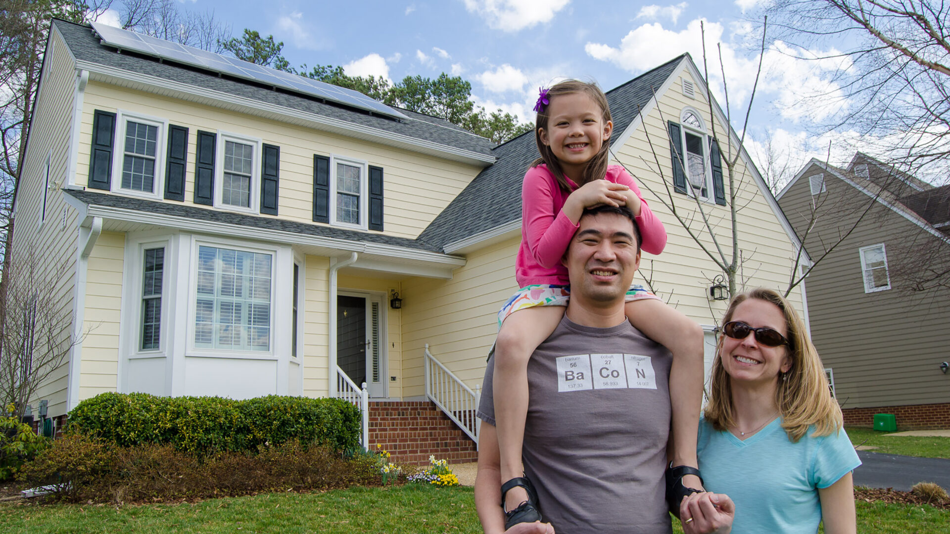 A family smiling in front of their solar home.