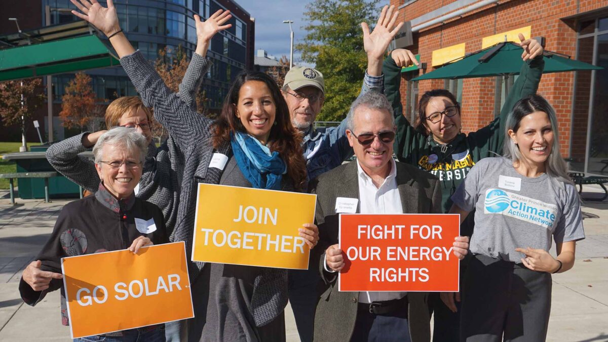 group of seven people with hands in the air and signs that say: go solar, join together, fight for our energy rights