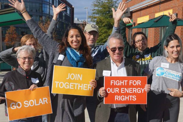 group of seven people with hands in the air and signs that say: go solar, join together, fight for our energy rights