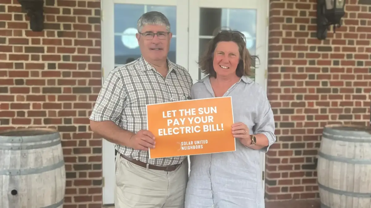 Man and woman holding sign that reads "Let the sun pay for your electric bill!"