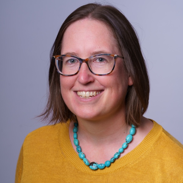 headshot of Liz wearing yellow shift and turquoise necklace