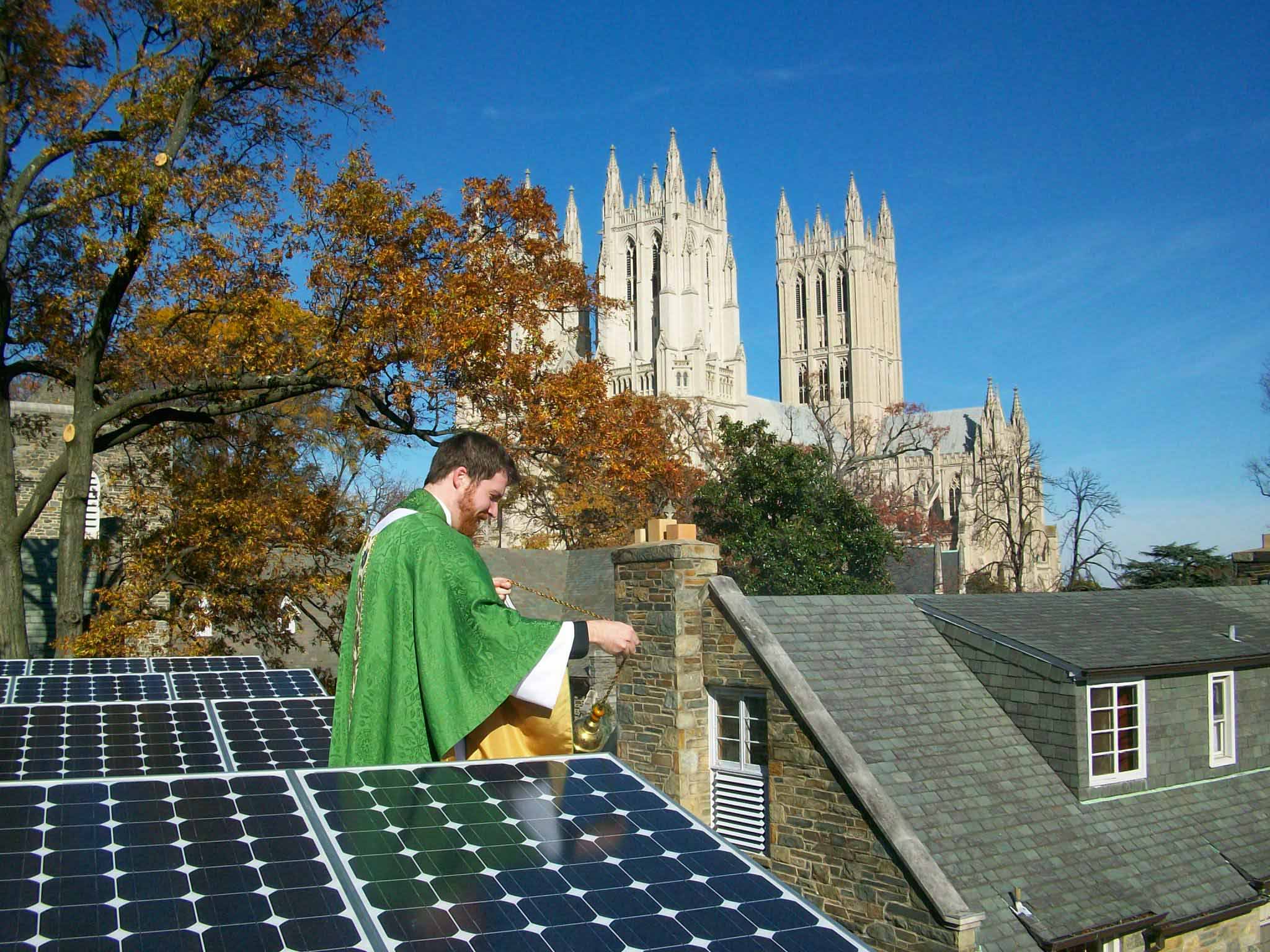 An Episcopal priest burns incense over a row of solar panels. A large cathedral is in the background.