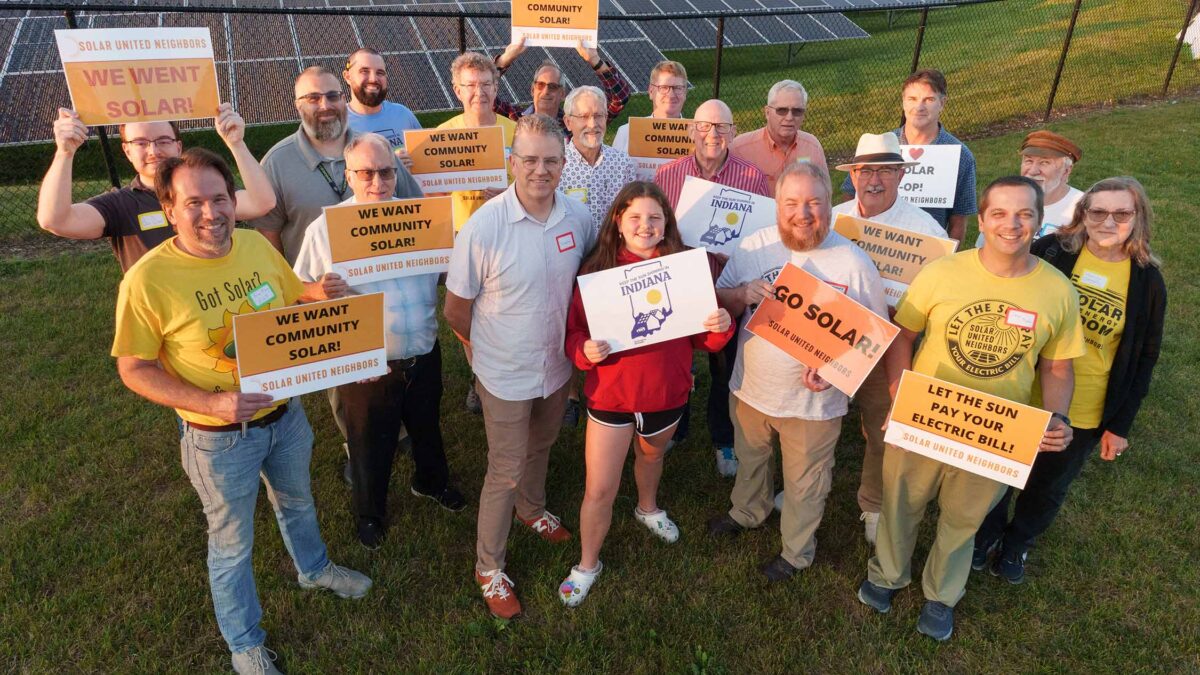 Group of people in a field standing in front of solar panels.