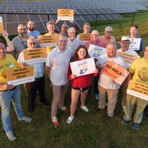 Group of people in a field standing in front of solar panels.