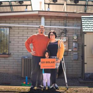 Family of man, woman, and young girl standing in the backyard of their house with rooftop solar panels installed.