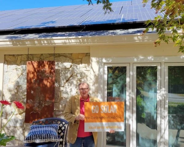 Man standing in his backyard holding a "Go solar" sign.