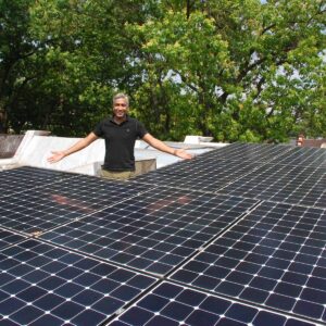 Man with his arms out standing behind large solar panels.