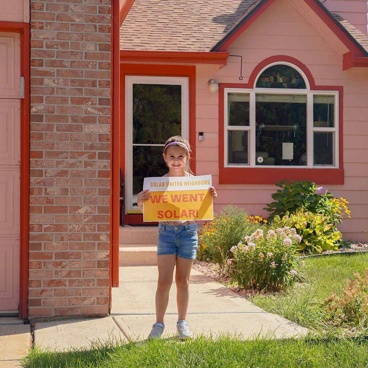 Young girl holding "We went solar" sign in front of pink house.