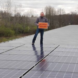Man holding "We went solar!" sign standing between solar panels in a field.