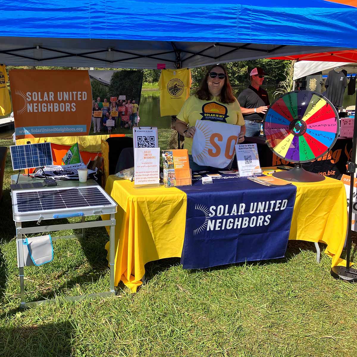 Woman standing under tent in a park tabling for an event.