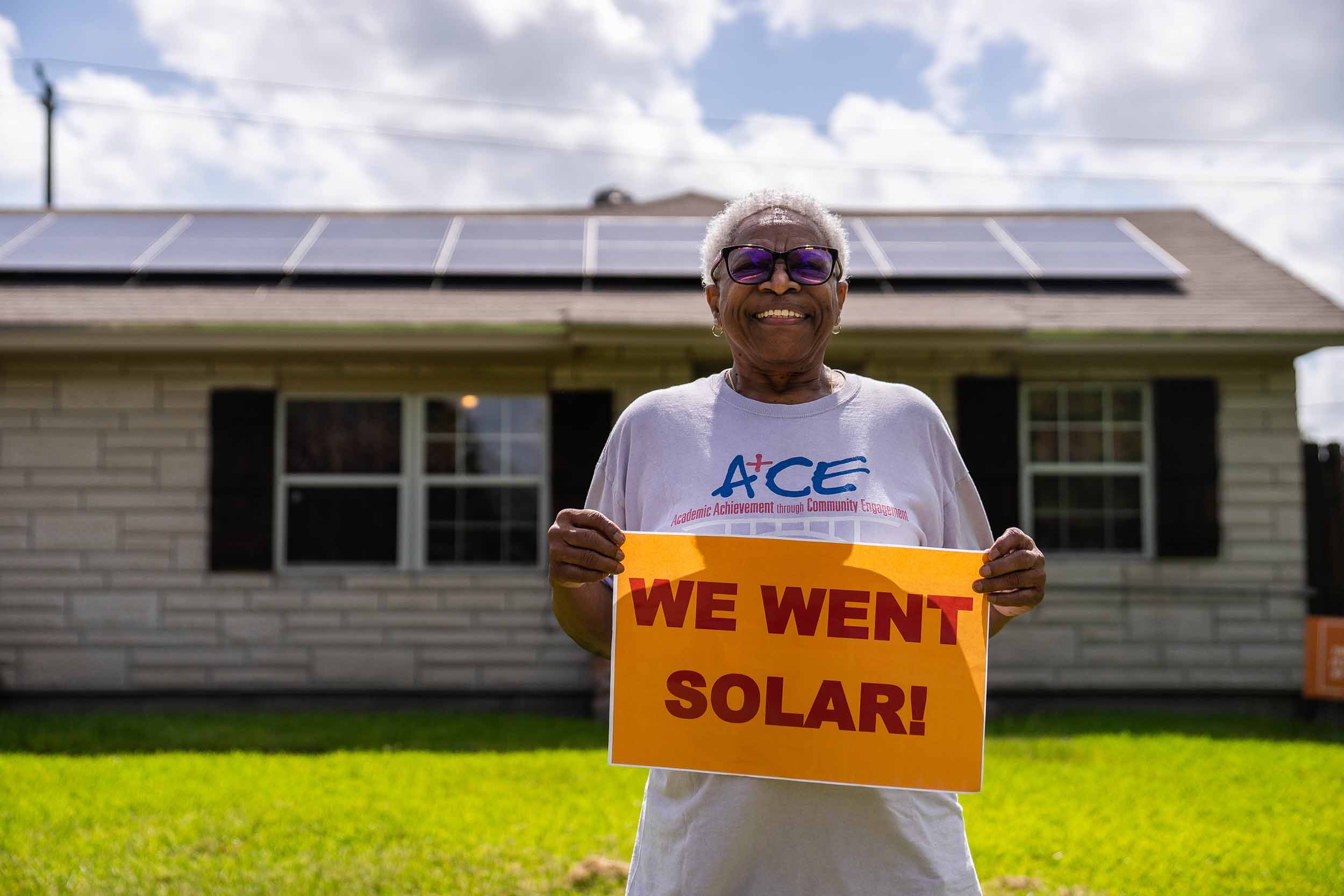 Woman standing in her backyard holding a sign that reads "We went solar!"