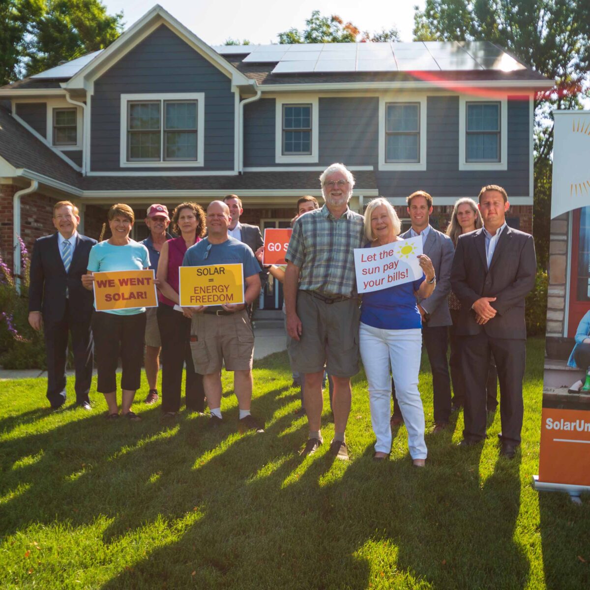 Group of people standing in front of a house with rooftop solar panels.