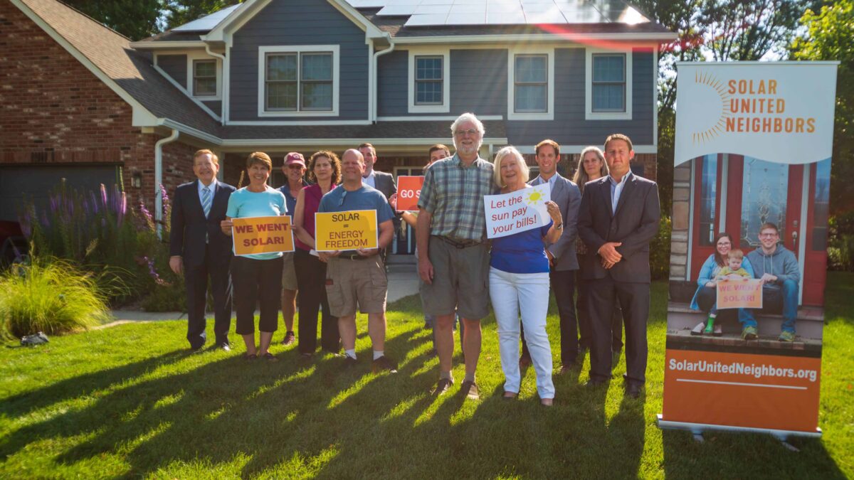 Group of people standing in front of a house with rooftop solar panels.