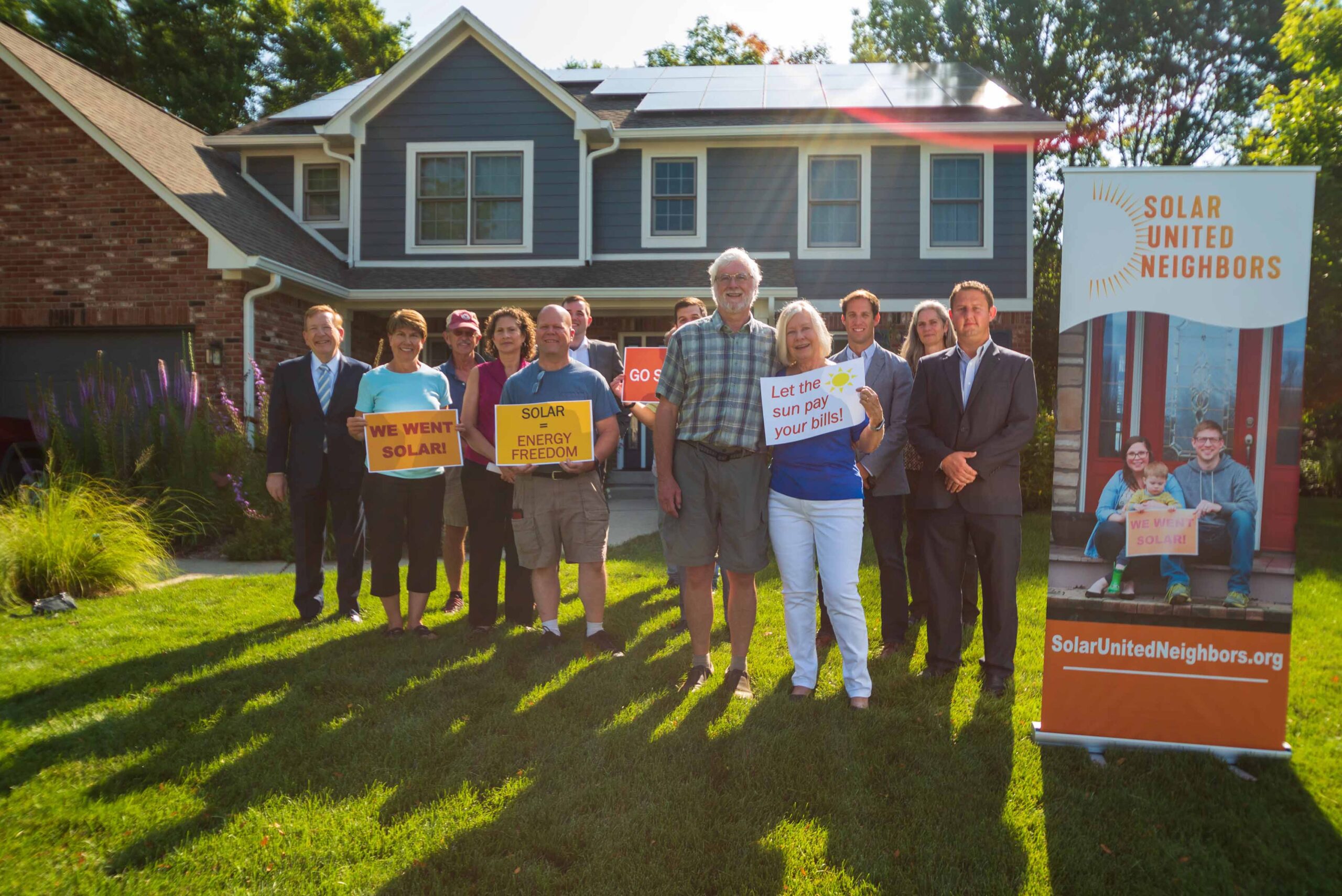 Group of people standing in front of a house with rooftop solar panels.