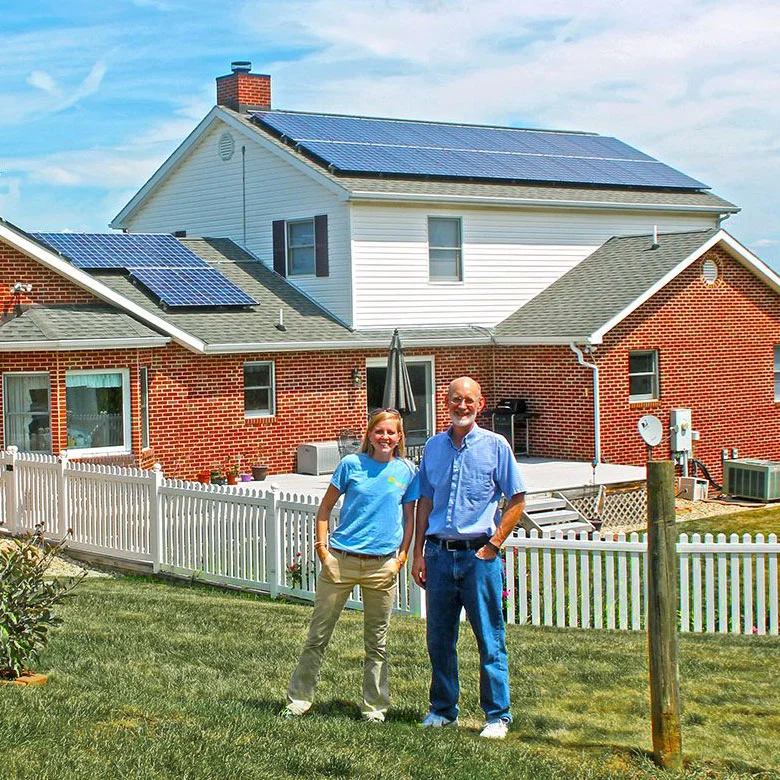 Husband and wife standing in front of brick house with many solar panels installed on rooftop.