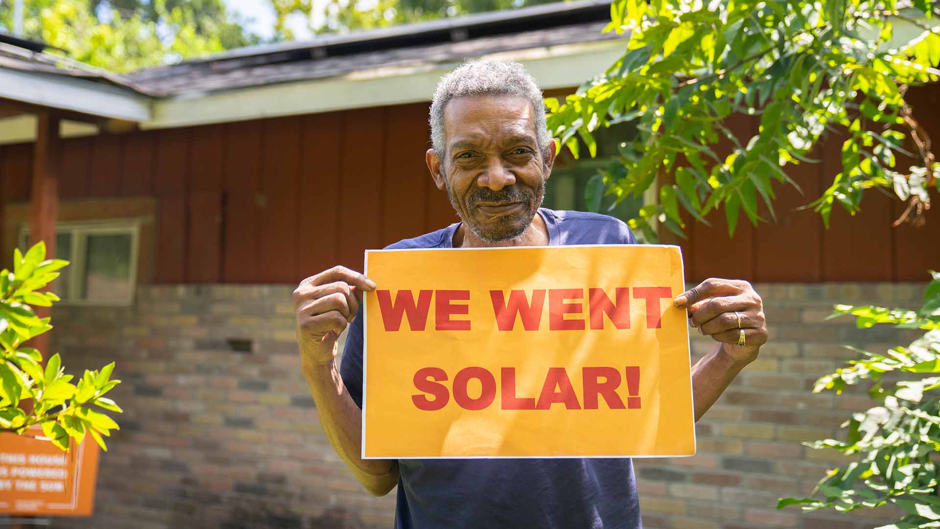Man holding "We went solar!" sign in a backyard.