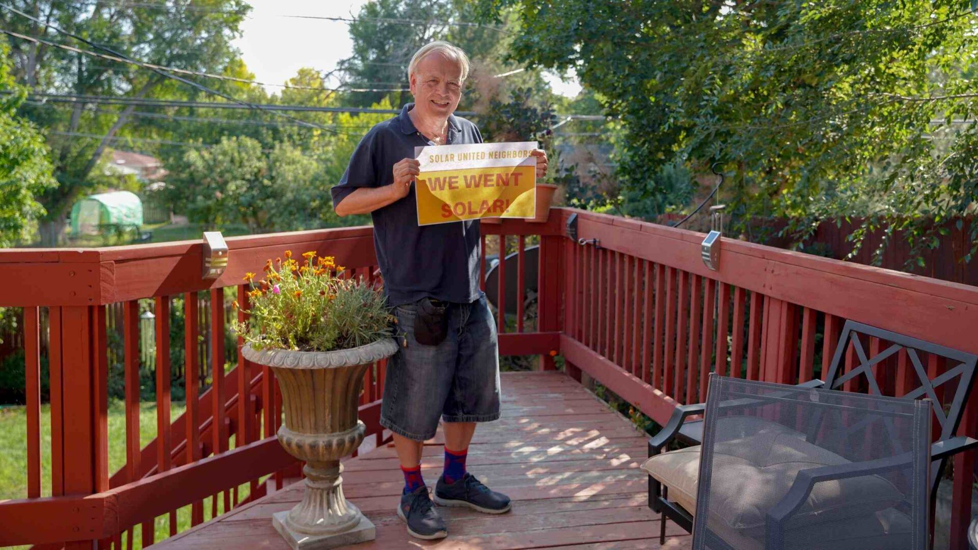 Man standing on backyard deck holding sign that reads "We went solar!"