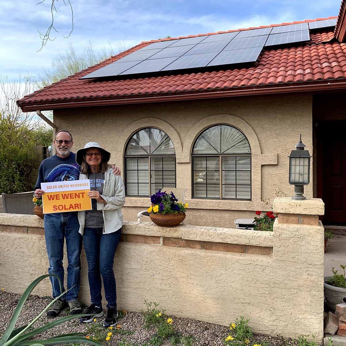 Husband and wife standing in front of home with rooftop solar panels.