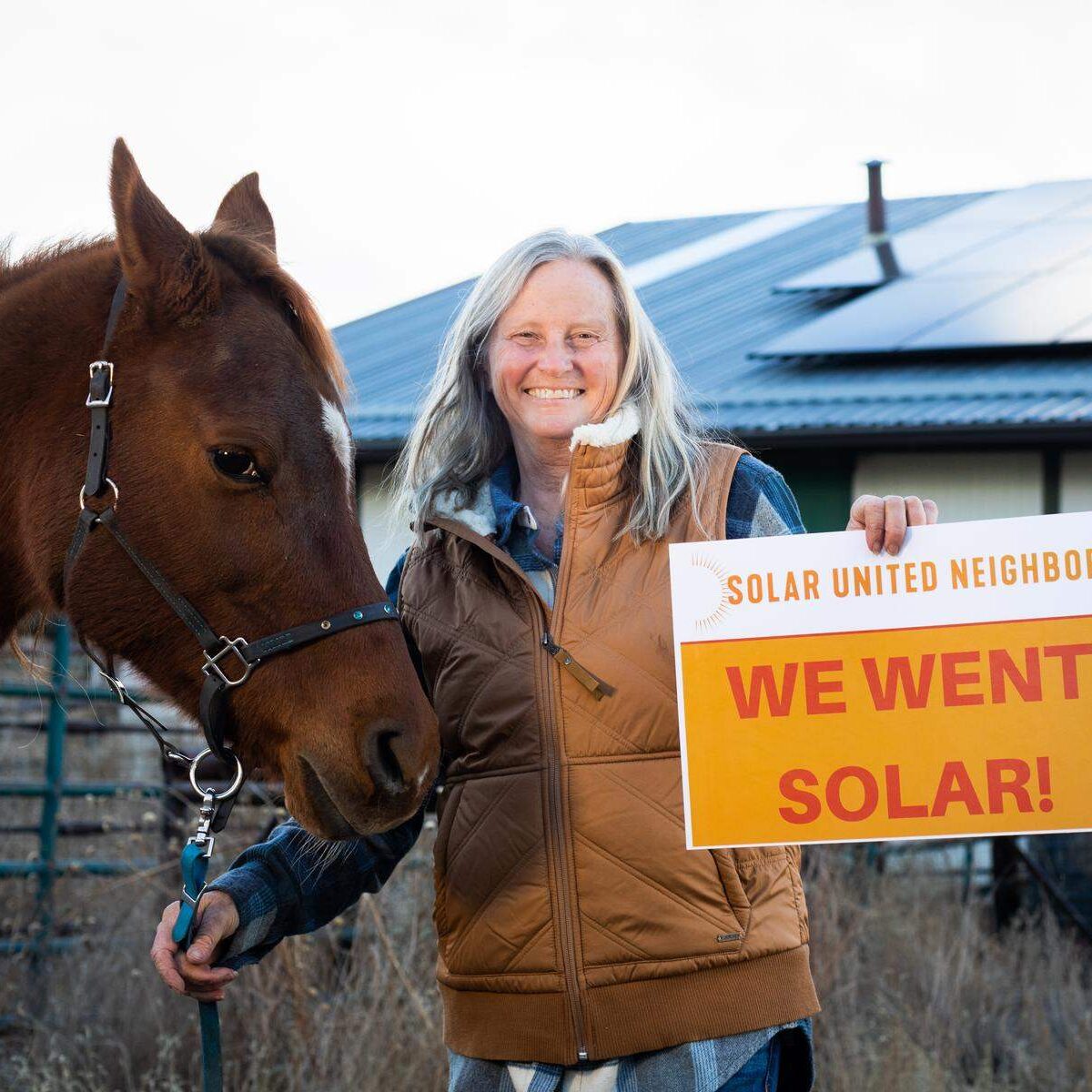 Woman standing next to horse on farm with a "We went solar sign" in her hands.