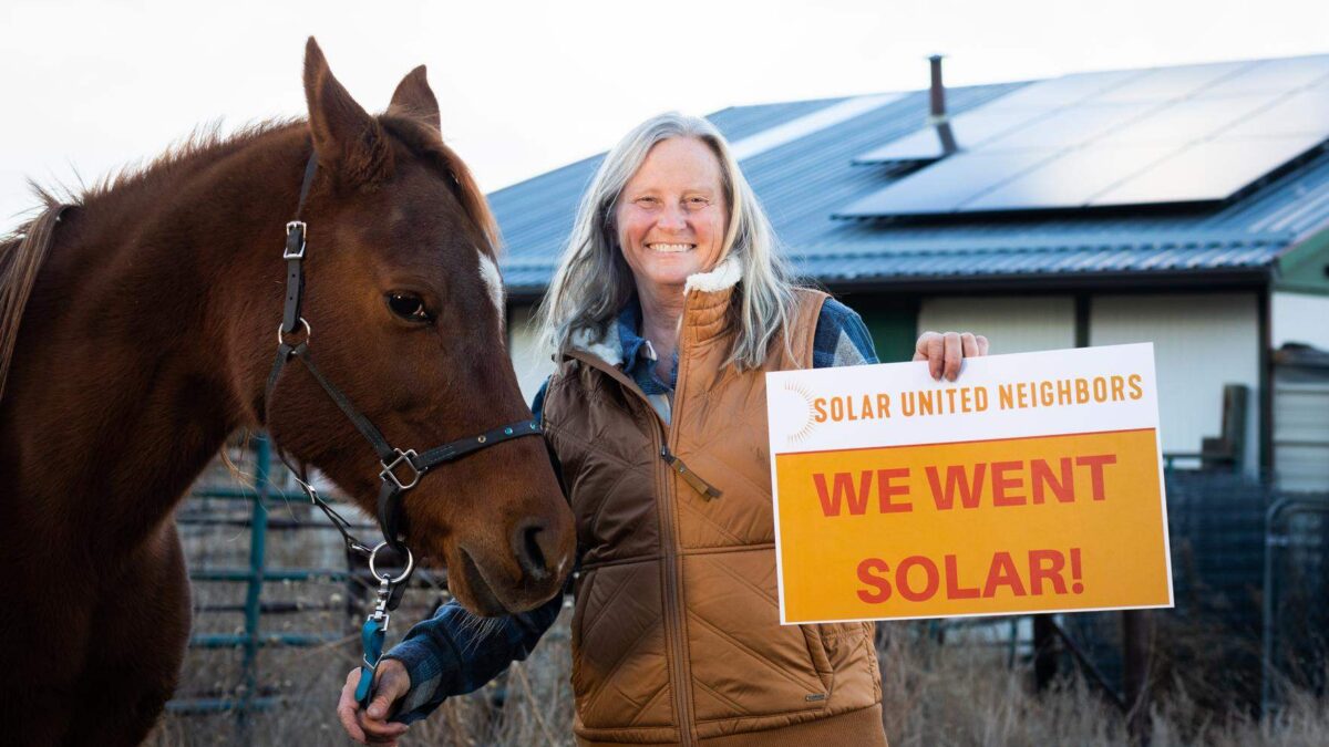 Woman standing next to horse on farm with a "We went solar sign" in her hands.