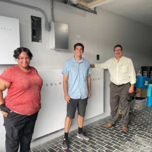 Three people standing next to Tesla batteries.