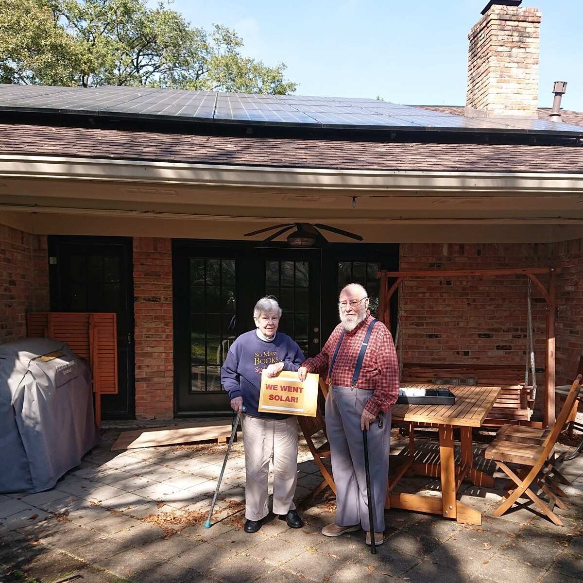 Older couple standing in front of house with solar panels on roof.