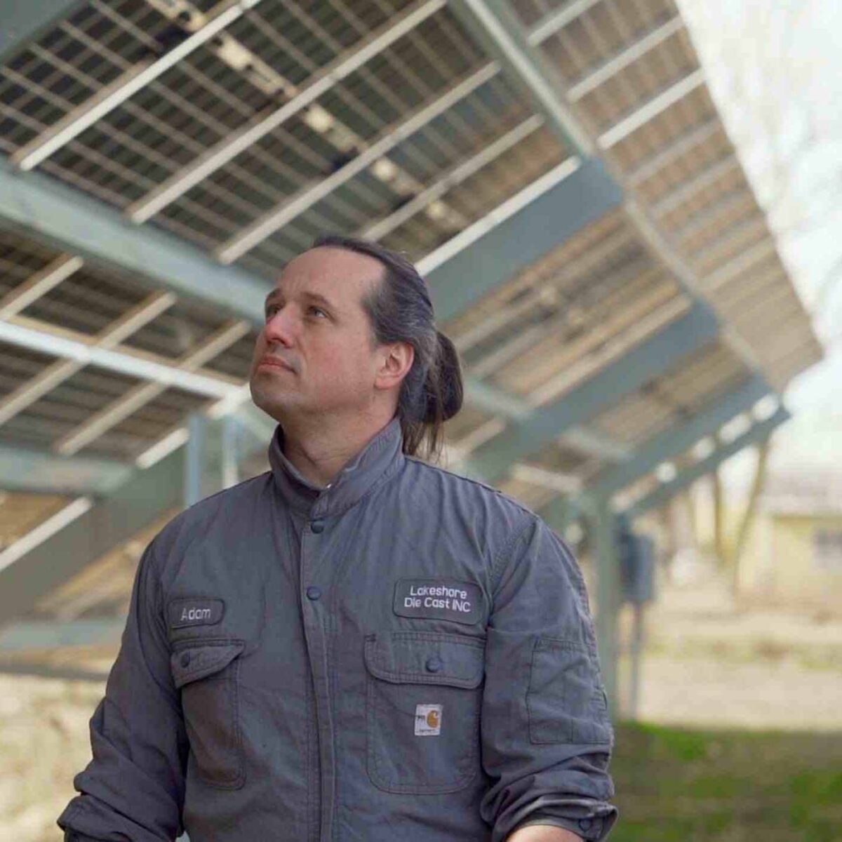 Man standing under solar panels in a field.