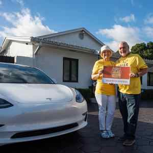 Couple standing next to an electric vehicle.