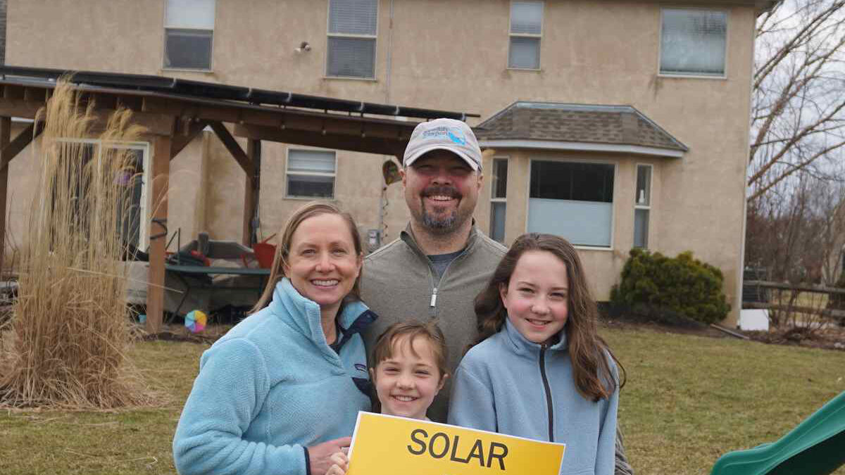 Family of four holding a "Solar equals energy freedom" sign.