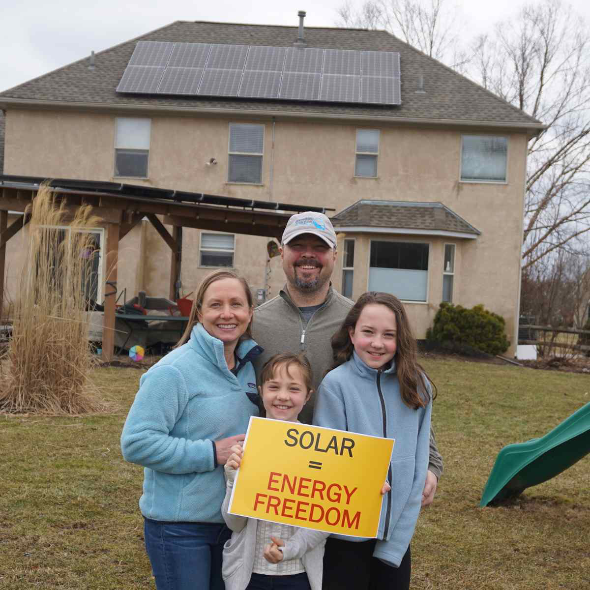 Family of four holding a "Solar equals energy freedom" sign.