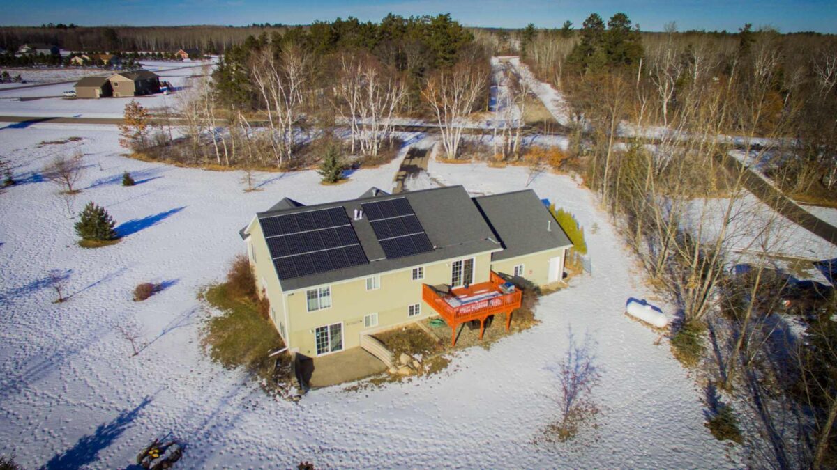 Aerial view of a home with solar panels during the winter and snow is on the ground.