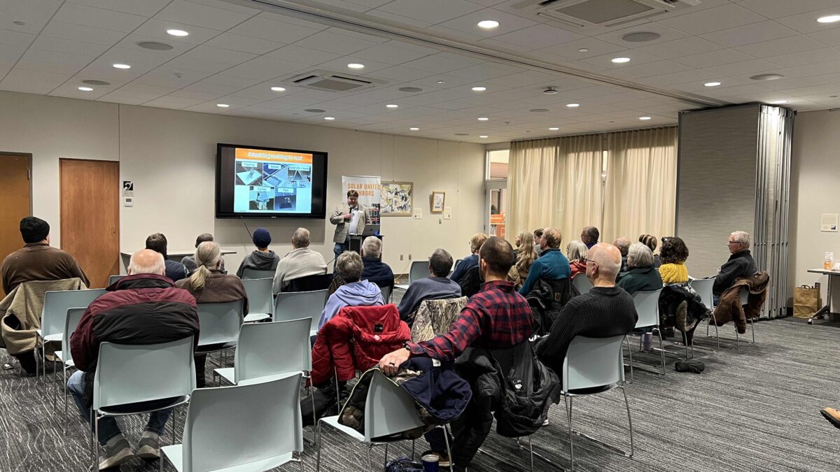 John Anderson presenting a Solar 101 presentation to a group of seated people indoors.