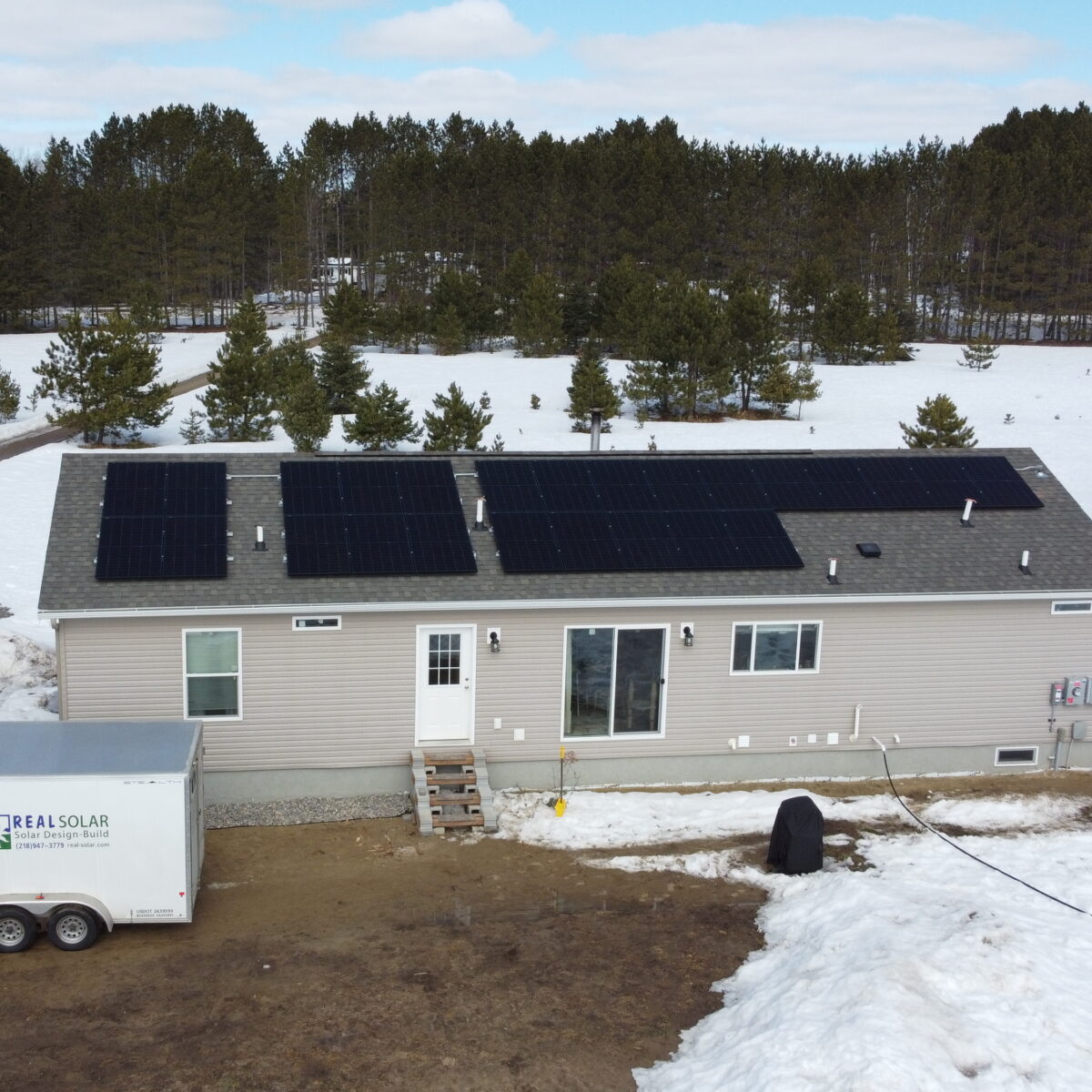 White home with rooftop solar with snow and trees around it.