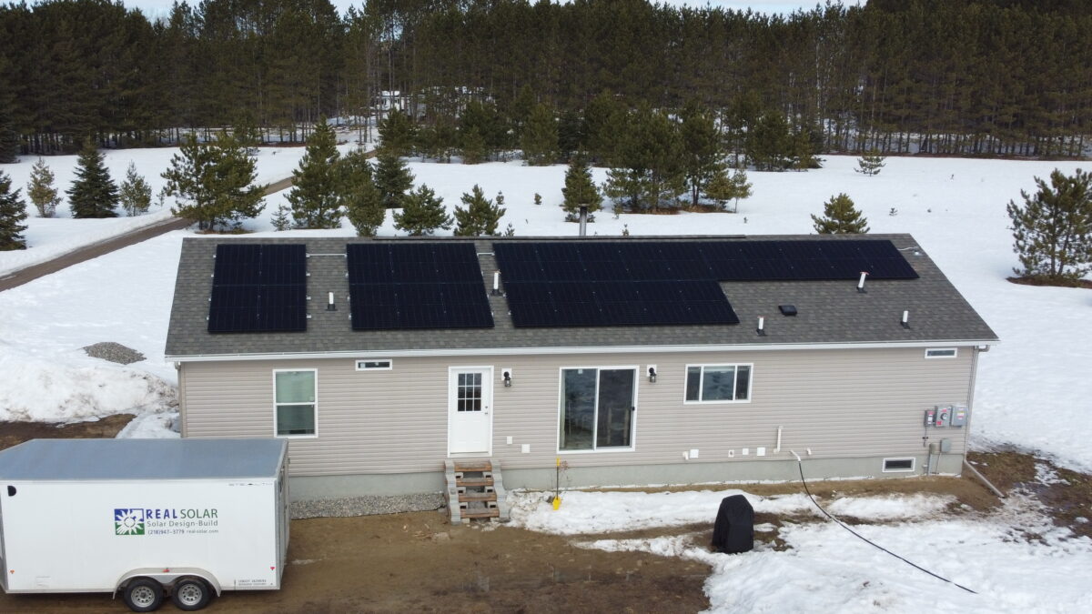 White home with rooftop solar with snow and trees around it.