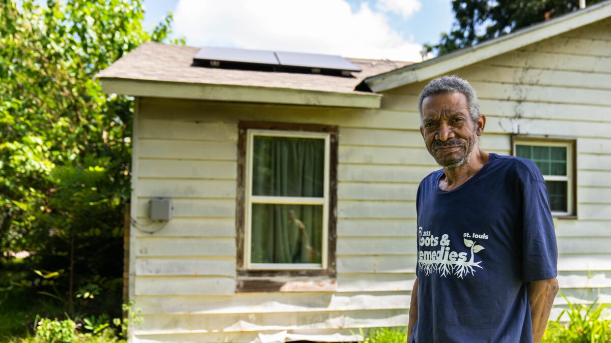 Person standing in front of a solar home and smiling.