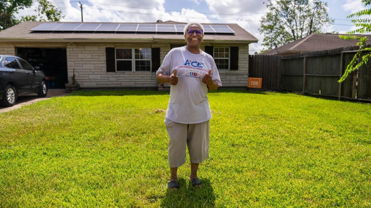 Person standing in front of a solar home and smiling.