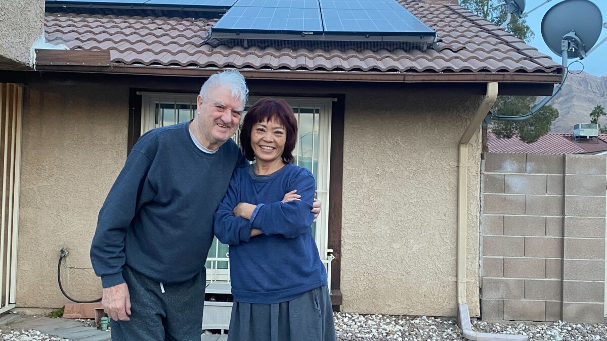 Two homeowners posing in front of their house with rooftop solar.