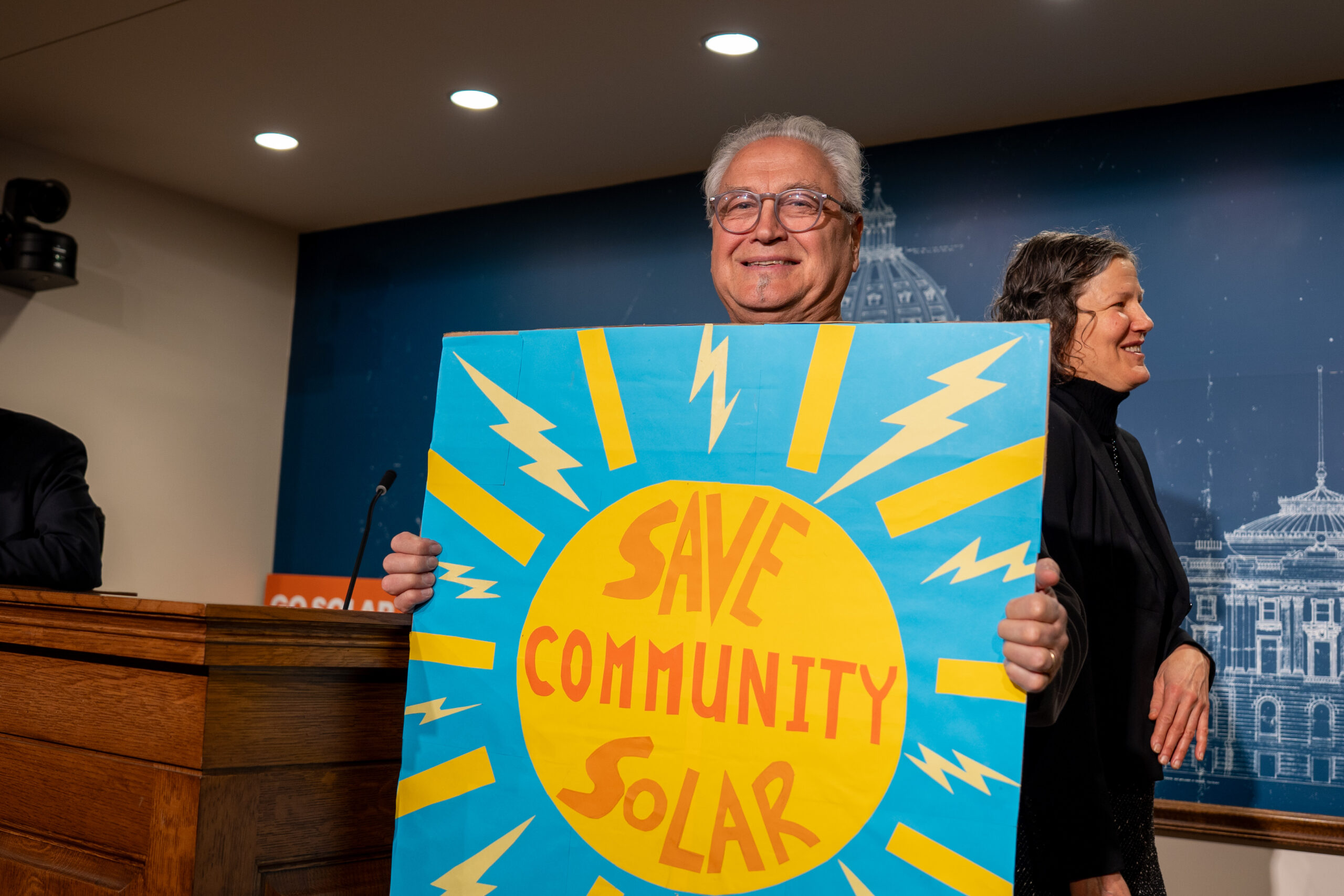 A man smiling and holding a sign that says "save community solar"