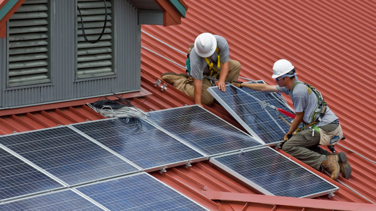 Two workers installing solar panels on a roof