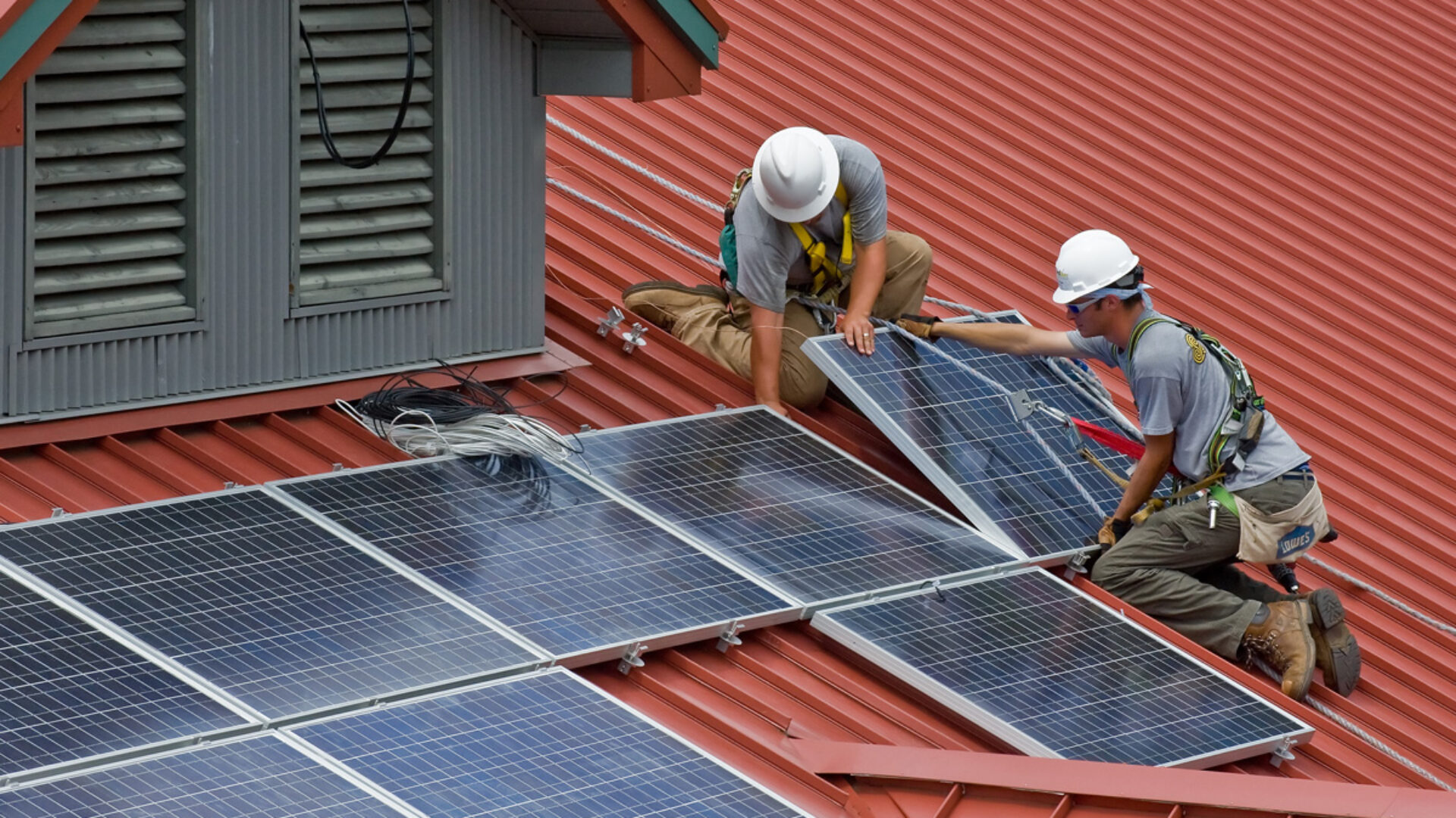 Two workers installing solar panels on a roof