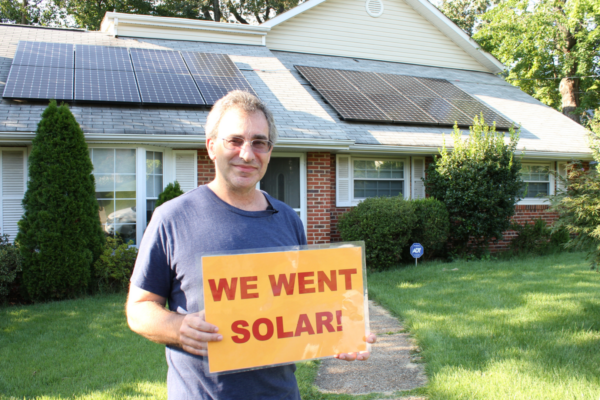 Person holding a "We Went Solar" sign in front of their solar home