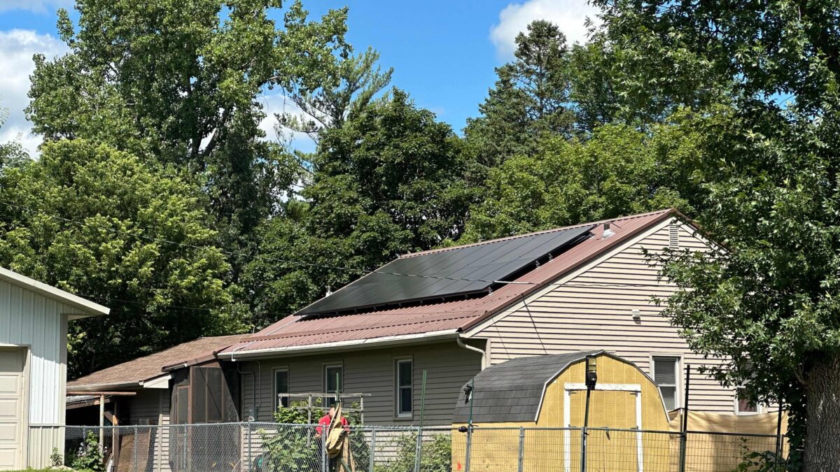 One story house with rooftop solar and a yard of trees behind it.