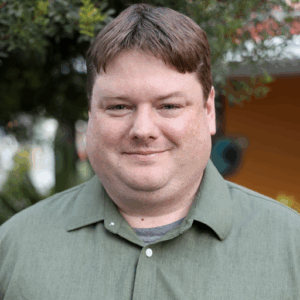 Headshot of John Anderson, Minnesota Program Associate, smiling in a sage green shirt and nature background.