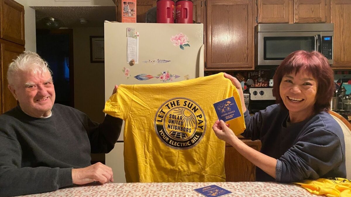 Larry and Angie Johnson smiling and holding a SUN shirt and sticker.