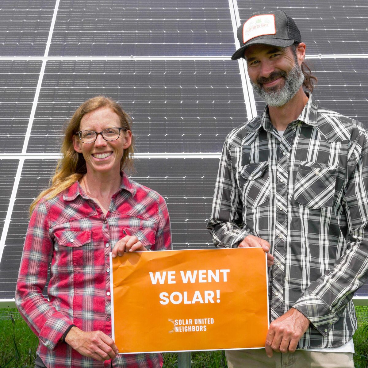 Two smiling solar co-op members stand in front of their ground mount system.