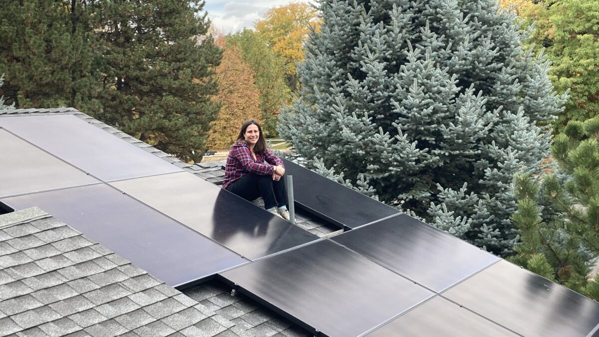 Smiling homeowner sitting on roof with installed solar panels.
