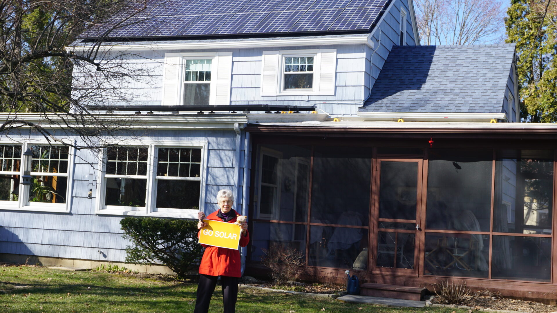 Solar owner standing in front of their home with solar panels, holding a sign that reads "Go Solar".