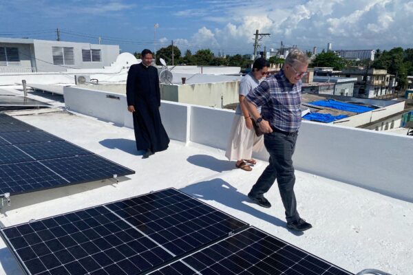 a priest and two others walking by solar panels installed on a flat, white roof in Puerto Rico