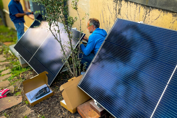 2 people installing plug in solar panels beside a building